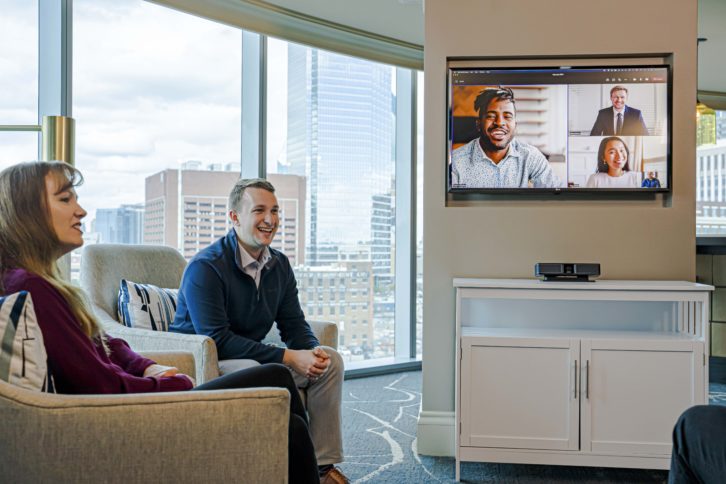 Two people sitting smiling in front of display and Bose Soundbar.