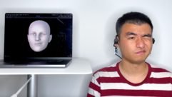 Man winking while wearing EarIO, next to a monitor displaying a computer-modeled head also winking