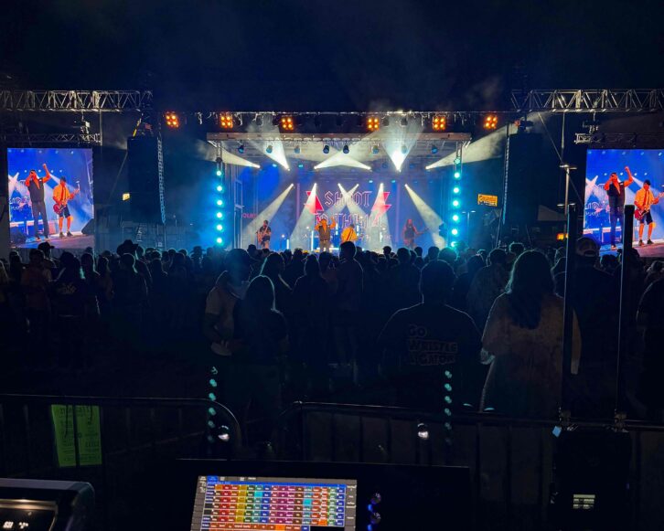 Nighttime festival performance viewed from front of house, with a large audience, illuminated stage, video screens, and flown DAS Audio sound systems.
